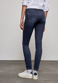 Mörkblå denim skinny jeans med en klassisk femficksdesign, subtil sömnad och midja med medelhöjd, i kombination med vita sneakers.