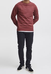 Felpa girocollo bordeaux con maniche lunghe, in tessuto strutturato, abbinata a pantaloni scuri e sneakers nere con righe bianche.