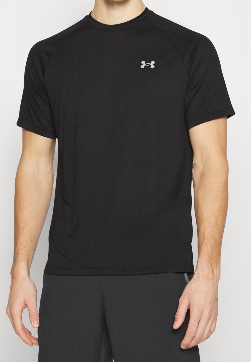 Svart kortärmad sporttröja tillverkad av mjukt, lätt tyg med rund hals och en liten grå logotyp på vänster bröst.