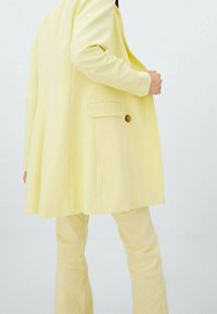 Gele oversized blazer met een enkele knoop, zijzakken en een gladde textuur, gecombineerd met bijpassende uitlopende broek.