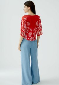 Rotes floral gemustertes Oberteil mit lockerer Passform und weiten Ärmeln, kombiniert mit hellblauen weitem Jeans. Der Stoff wirkt leicht und atmungsaktiv.