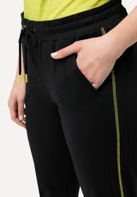 Zwarte joggingbroek met een elastische tailleband, trekkoord, zijzakken en gele stikaccenten langs de buitennaden.