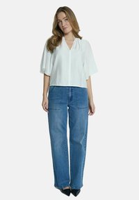 Bílá krátkosrstá blůza s výstřihem do V v kombinaci s modrými širokými džíny. Outfit má volný střih a minimalistický design.