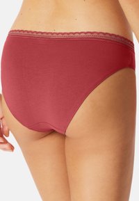 Rote Baumwollmischung-Bikiniunterwäsche mit gewelltem Spitzenbesatz. Sie verfügt über eine glatte Textur und klassische Briefform, sichtbar aus einem Seitenwinkel.