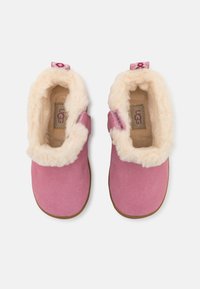 Chaussons en suede rose avec une doublure blanche duveteuse, dotés de fermetures à crochets et boucles et d'un design à bout rond. Marque UGG visible à l'intérieur.