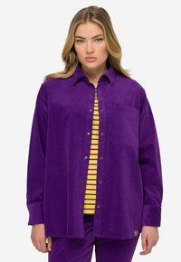 Violetti corduroy-paita napakolla, rinta-tasku ja nepparit. Päällä kelta-valko-raitaista puseroa.