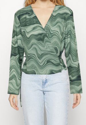 Groen gemarmerde wikkeltop met lange mouwen, met een diepe V-hals en zijbanddetail. Gecombineerd met lichtblauwe denim jeans.