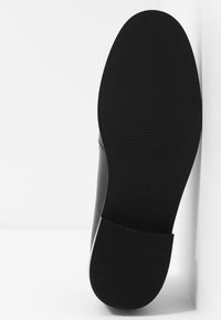 Semelle de chaussure de ville noire avec talon texturé et semelle lisse, vue de dessous sur un fond blanc.