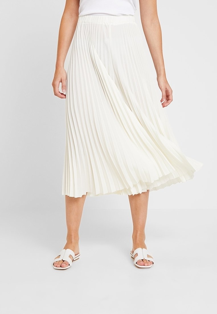 Jupe midi plissée en tissu blanc cassé, avec une ceinture ajustée. Le design présente une texture fluide qui accentue le mouvement.