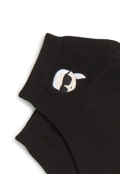 Chaussettes noires ornées d'un visage de dessin animé brodé blanc portant des lunettes de soleil, fabriquées dans un matériau doux et texturé. Deux paires présentées.