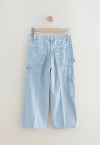 Pantalons cargo rayés bleus et blancs, dotés de multiples poches et d'une coupe décontractée, fabriqués en tissu léger. Accrochés à un cintre en bois.