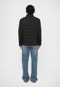 Jachetă puffer neagră cu design capitonat orizontal, textură moale, guler înalt și asociată cu blugi largi de culoare albastru deschis.