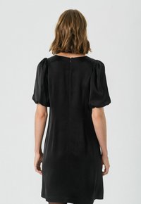 Rochie scurtă neagră cu mâneci bufante, textură fină, decolteu rotund și detaliu cu fermoar la spate. Siluetă simplă și ajustată.