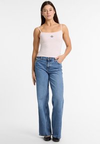 Débardeur rose à rayures avec des bretelles fines, présentant un petit motif d'étoile, associé à un jean bleu ample et des chaussures noires. Design simple, look décontracté.