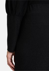 Zwart jurkje met een textuurstof, voorzien van lange mouwen en een gathered deel bij de schouders. Inclusief een discrete achterzak.