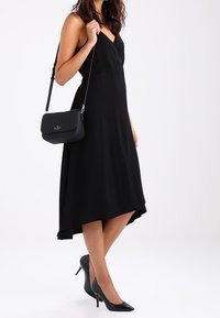 Černé áčkové šaty s výstřihem do V a asymetrickým lemem. Doplnené černými jehlovými podpatky a malou černou kabelkou s ramenním popruhem.