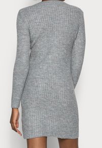 Grå ribbad stickad klänning med långa ärmar, figurnära passform, rundad halsringning och en något rundad nederkant. Tyget verkar mjukt och strukturerat.