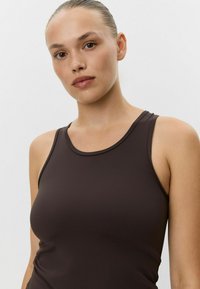 Hnedý priliehavý top na ramienka s okrúhlym výstrihom a širokými ramienkami. Vyrobený z hladkej tkaniny, má bezšvový dizajn a minimálne švy.