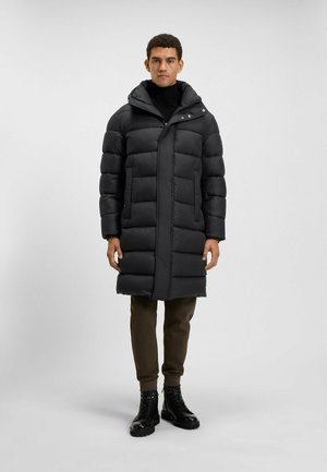 Black puffer coat features a quilted design, high collar, and front snap closures. Worn with olive green pants and black lace-up boots.
