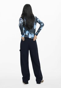 Top cu mâneci lungi, dungat în albastru și negru, cu modele abstracte; asortat cu pantaloni negri largi, prevăzuți cu două buzunare în spate și accente metalice laterale.