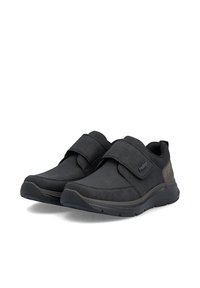 Paire de chaussures décontractées noires avec larges bandes auto-agrippantes et semelles coussinées, conçues pour le confort et la facilité d'enfilage.