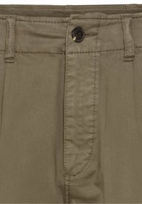 Gros plan sur la ceinture d’un pantalon couleur kaki avec passants de ceinture, un bouton noir et une braguette zippée cachée avec des coutures visibles.