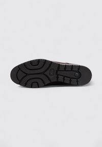 Suela de goma negra con patrón de agarre texturizado, que presenta surcos profundos y un detalle de logotipo circular cerca del talón.