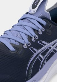 Tumeda laevansinise värvusega jooksujalatsid, millel on helelillat värvi aktsendid, tekstureeritud pealiskate, pehmendusega keel ja kangasist paelad. Paistavad silma logoga ja silmarkinnitustega.