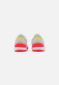 Zapatillas deportivas grises con acentos en neón rosa y amarillo, textura de malla en el talón y logo de tres franjas prominente en los lados.