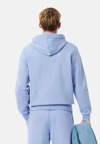 Haut à capuche bleu clair avec poche kangourou, poignets et ourlet côtelés. Texture lisse, capuche avec cordon de serrage, associé à un pantalon de jogging assorti et une veste en denim.