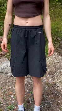 Personne debout à l'extérieur portant un short cargo noir et un débardeur court marron avec des chaussettes blanches et des baskets sur un sol rocheux.