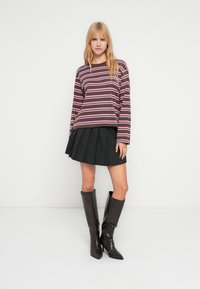 Ριγέ πουκάμισο μακρυμάνικο σε σκούρο καφέ με ροζ και λευκές ρίγες, συνδυασμένο με πλισέ μαύρη φούστα και μαύρες μπότες μέχρι το γόνατο.