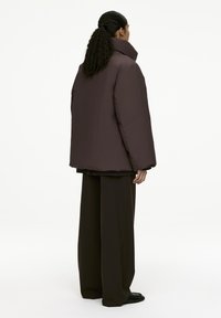 Dark brown, oversized puffer jacket with a high collar, smooth texture, and angular shape, paired with wide-leg dark trousers.