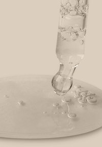 Contenitore trasparente con un'estremità rotonda, che rilascia un liquido chiaro su una superficie bianca lucida, circondato da piccole bolle e gocce.