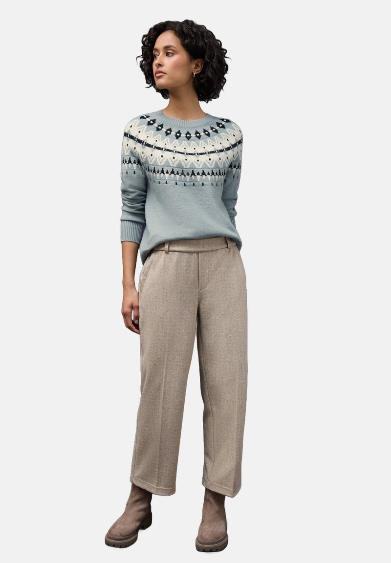 Maglione azzurro chiaro con motivo Fair Isle al colletto, abbinato a pantaloni a quadri beige e stivaletti taupe alla caviglia. Tessuti morbidi, vestibilità rilassata.