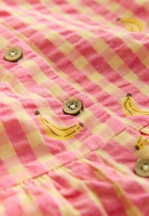 Roze en geel geruit stof met kleine banaanprints; voorzien van houten knopen en een geplooide zoom voor textuur en detail.