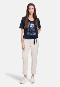 Marineblå kortærmet t-shirt med grafisk print, knyttet foran, parret med lyse beige tapered bukser og hvide sneakers.