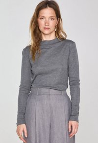 Graues Langarmoberteil mit hohem Ausschnitt, das eine weiche Textur aufweist. Kombiniert mit hellgrauen, gefalteten Hosen, die ein maßgeschneidertes Design zeigen.