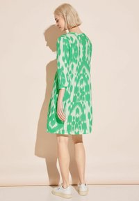 Grön mönstrad klänning med trekvartsärmar, lös passform och ett lagerdesign. Tyget har en strukturerad yta; bärs tillsammans med vita sneakers.