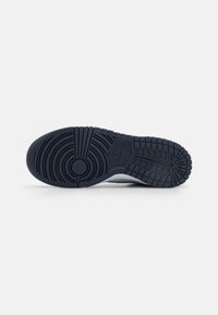 Navy-blue sneaker sole with circular and horizontal tread patterns. Textured material and prominent branding logo near the heel.
