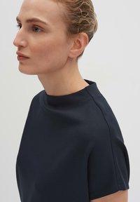 Marineblauwe top met korte mouwen en een hoge hals, gemaakt van een gladde stof. Heeft minimale stiksels en een ontspannen pasvorm.