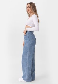 Lichtblauwe wijde jeans met een sterrenpatroon, hoge taille en vijf zakken, gecombineerd met een lange mouwen witte crop top.