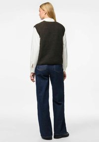 Tmavě zelená pletená vesta přes bílou košili, spárovaná s volnými tmavě modrými džíny. Obsahuje široký střih nohavic a dlouhé rukávy.