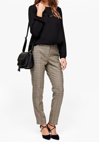 Blusa negra de manga larga con detalles de encaje, combinada con unos pantalones ajustados de cuadros en beige y marrón. Acabada con tacones negros con tiras y un bolso.