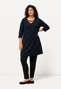 Marinefarbene Tunika mit V-Ausschnitt und Kreuzdetail, kombiniert mit schwarzen Leggings, abgerundet mit schwarzen Ballerinas. Weicher Stoff, knielanges Design.