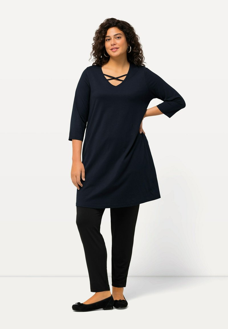Marinefarbene Tunika mit V-Ausschnitt und Kreuzdetail, kombiniert mit schwarzen Leggings, abgerundet mit schwarzen Ballerinas. Weicher Stoff, knielanges Design.