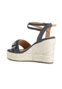 Sandali con zeppa in denim e piattaforma in juta intrecciata, caratterizzati da una fibbia decorata con gemme sulla cinghia e lacci incrociati alla caviglia di colore grigio scuro.