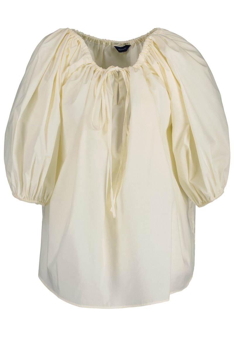 Blouse jaune pâle à coupe ample, manches bouffantes, poignets élastiques et encolure froncée avec un lien ajustable. Tissu en coton doux.