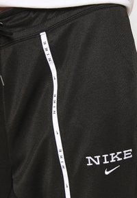 Svarta sportshorts med en slät textur, prydda med vitt Nike-logotyp och varumärkning längs sidan. Elastisk midja med snörning.