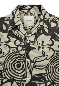 Hemd mit Knopfleiste aus strukturiertem Waffelstrickmuster in Hellgrün mit kräftigen schwarzen Blumenmustern und einem klassischen Kragen. Fünf weiße Knöpfe.